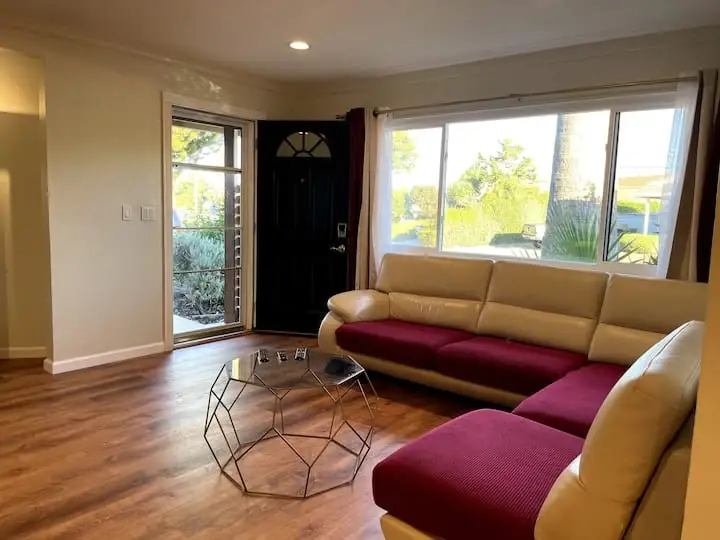 Cream sectional with burgundy covers beside the Serene home's garden-facing window